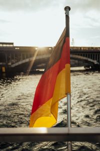 German flag waves against a scenic river and bridge backdrop during sunset, symbolizing national pride.